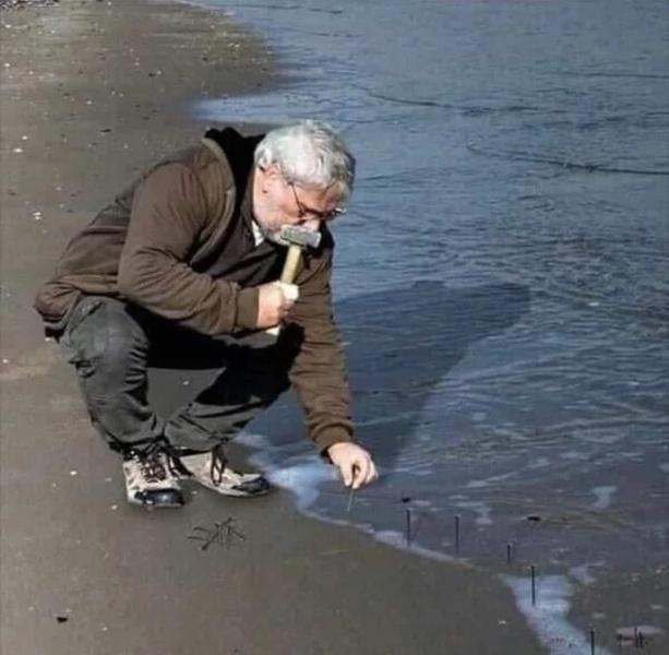 Guy Hammering Nails Into Sand